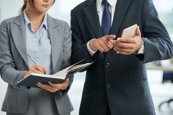 Studio Legale Rinaldi e Associati Avvocato in giacca e cravatta che punta allo smartphone in mano e una donna che prende appunti
