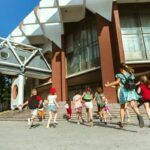 Bambini felici che giocano per strada in una soleggiata giornata estiva di fronte all'edificio moderno Le 10 Migliori Scuole Private di Roma
