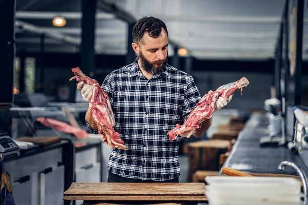 Bistecca di toro Macellaio barbuto vestito con una camicia di pile che lavora in macelleria